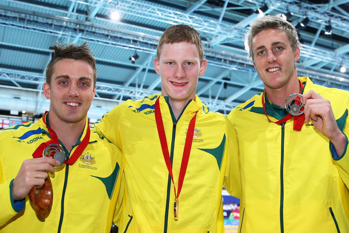 Three swimmers show their medals to the camera and smile