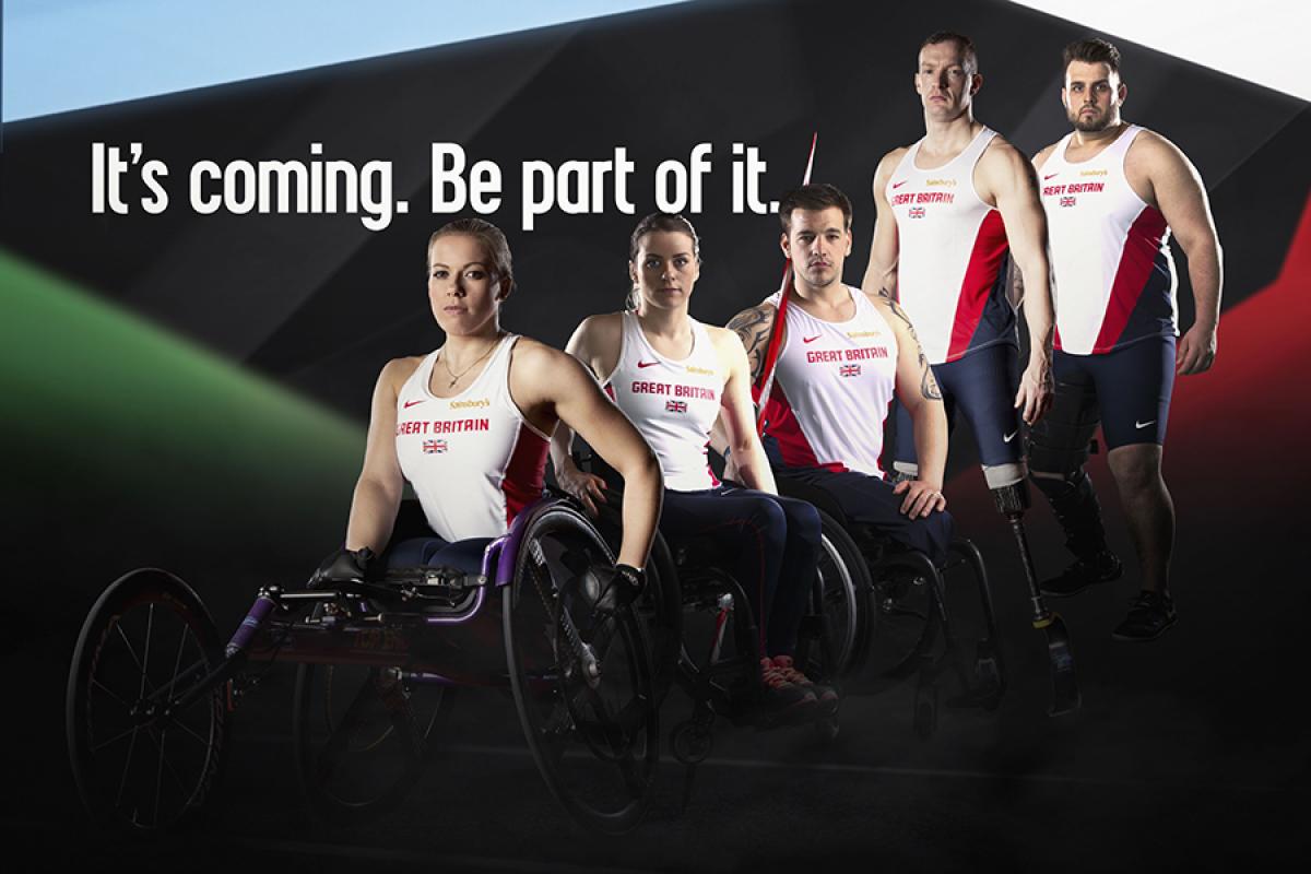 5 male and female athletes in British jerseys stand and sit (in wheelchairs) next to each others in front of a black wall. Behind them is the logo: Swansea 2014. It's coming. Be part of it. 