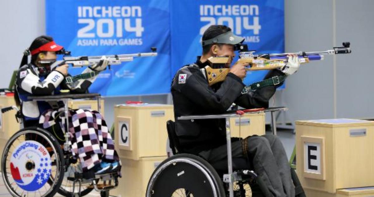 Two people in a shooting range, sitting in wheelchairs and targetting