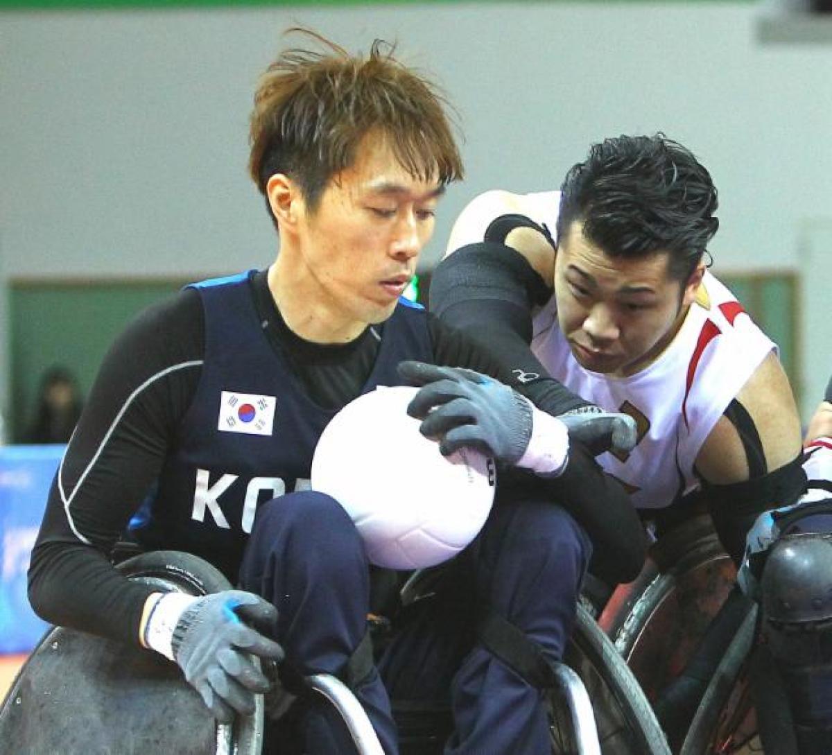 Two men in wheelchairs playing rugby, fighting for the ball