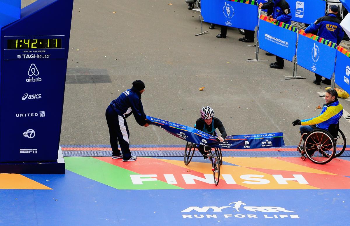 Women in racing wheelchair crosses the finish line on a street