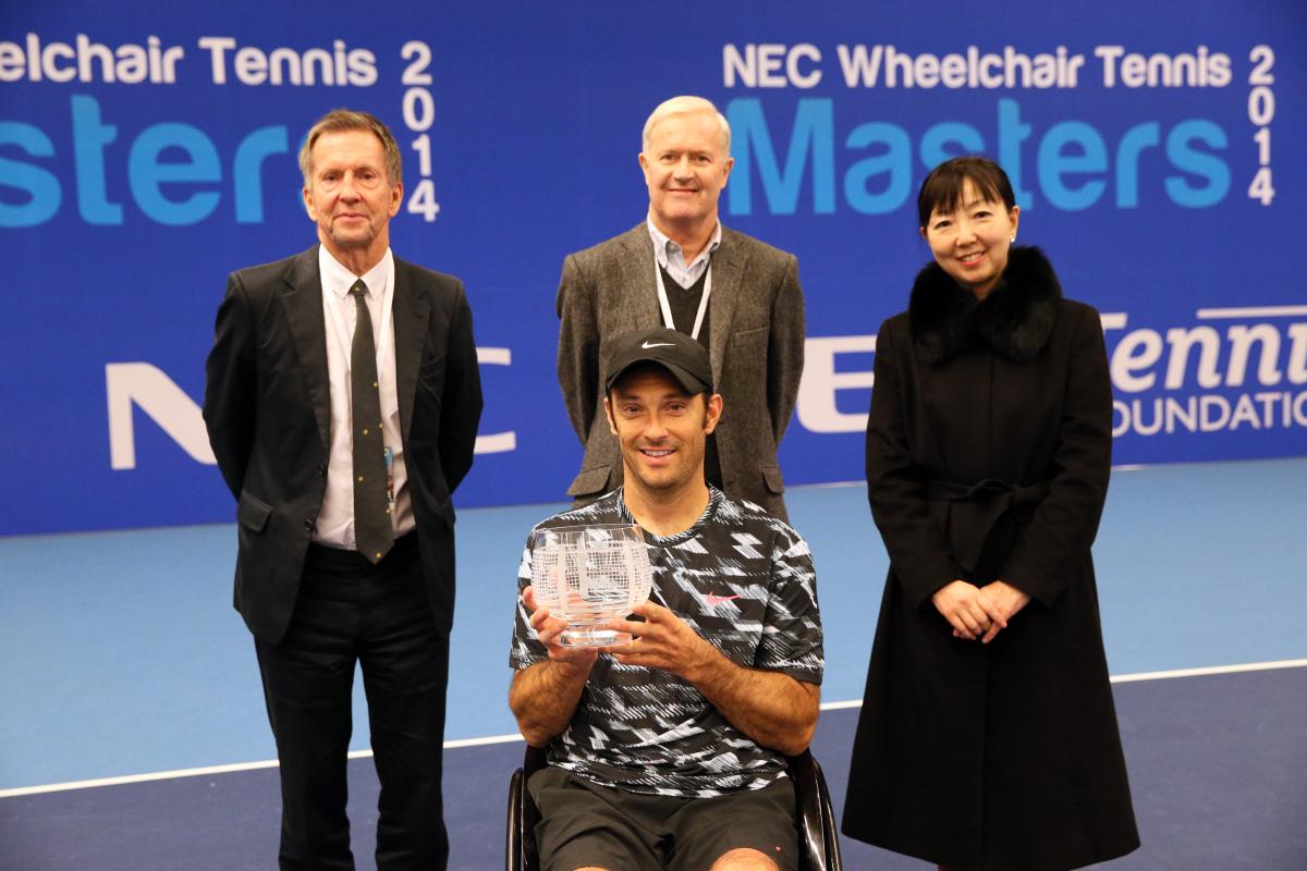 Man in wheelchair with tennis racket in triumphing pose