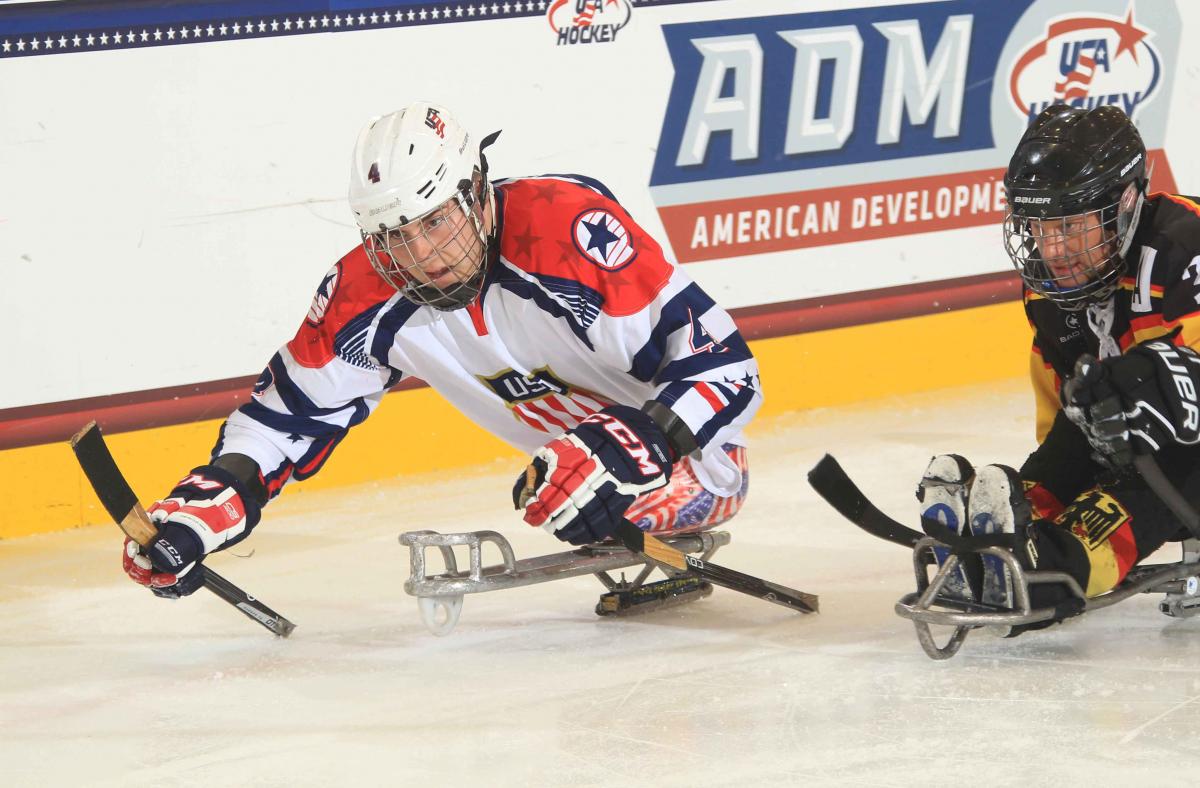 Two sledge hockey players chasing after the puck.