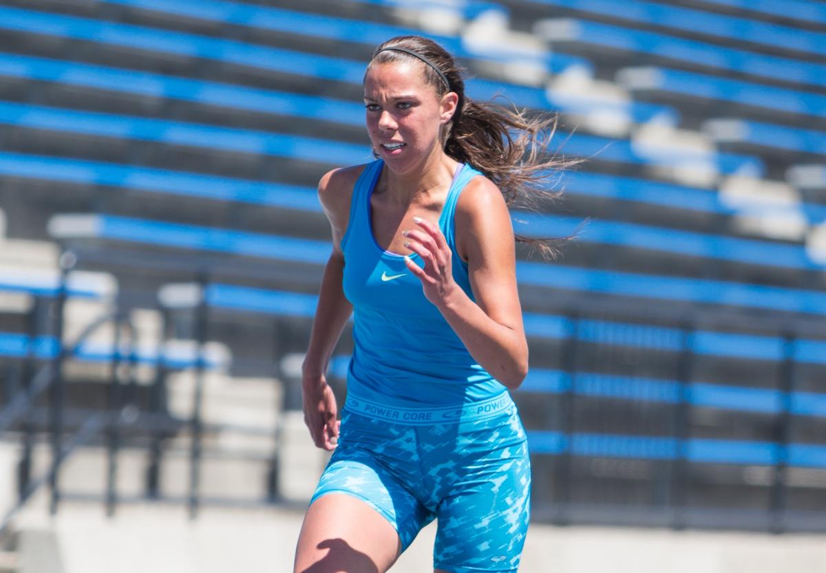 Women runs on a blue track, looks focused