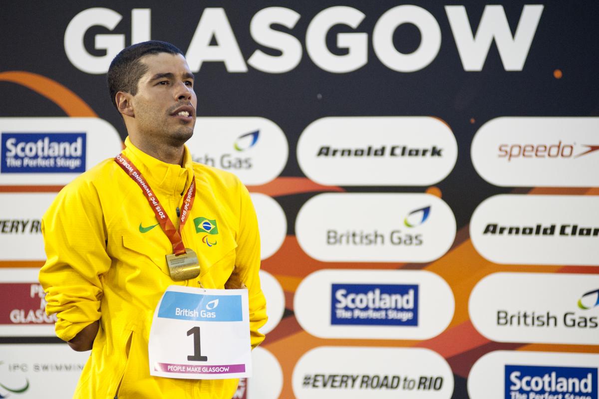 Man in yellow jacket standing ona podium, wearing a gold medal