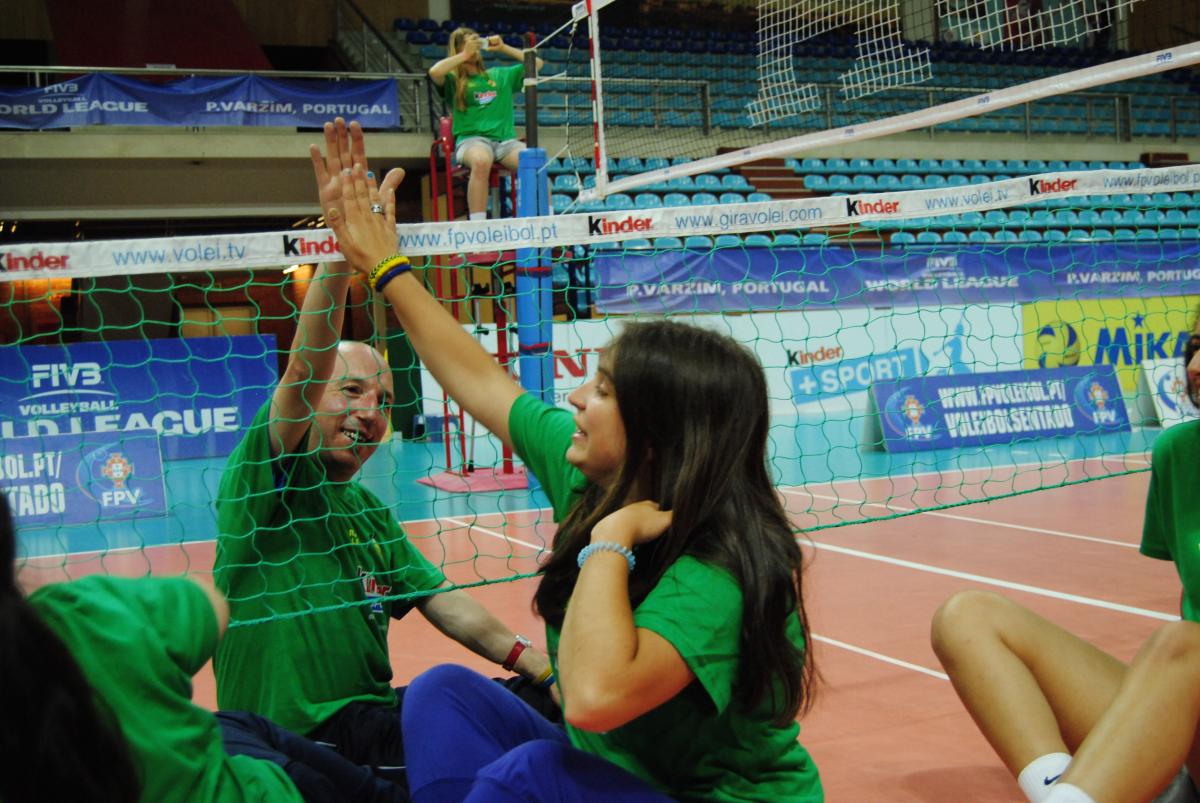 Girls and man doing high five, sitting on a volleyball field of play