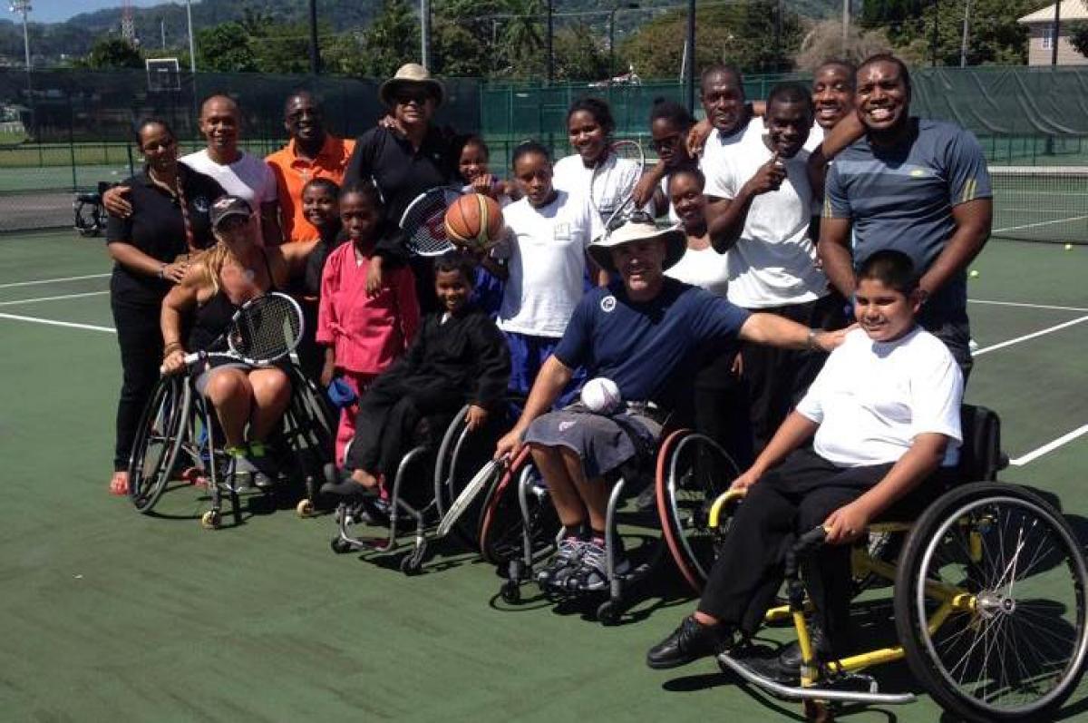 Group picture of people in wheelchairs and standing on a tennis court