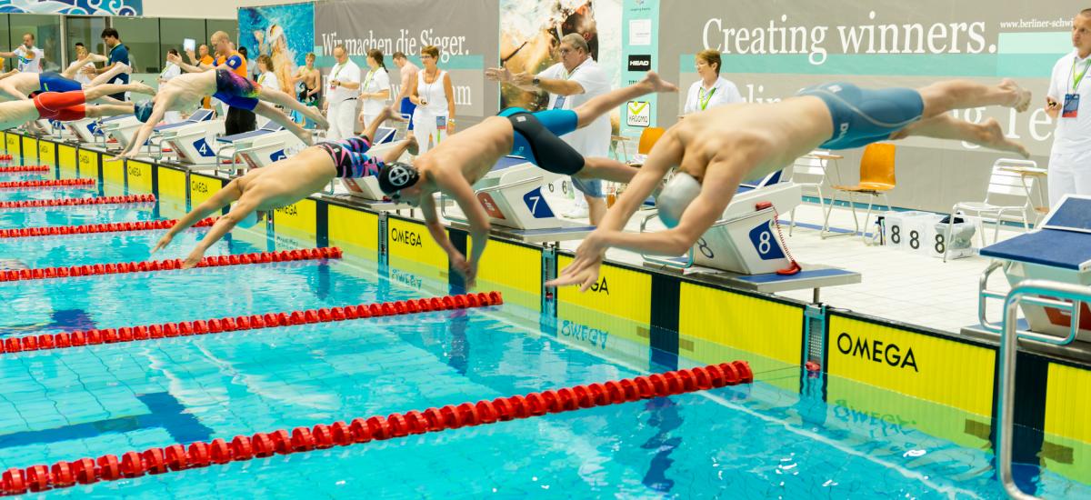 a group of male swimmers dive into the pool at the start of the race