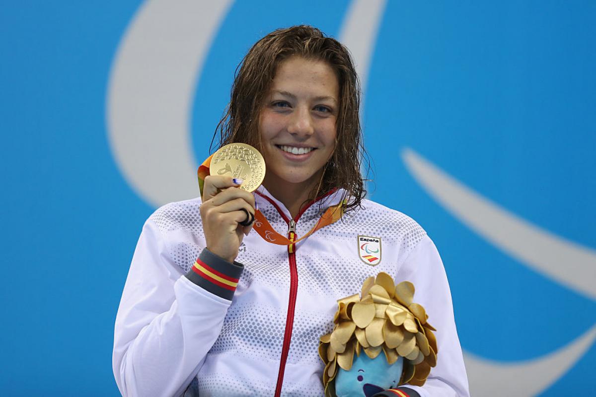 a female Para swimmer holds up her gold medal