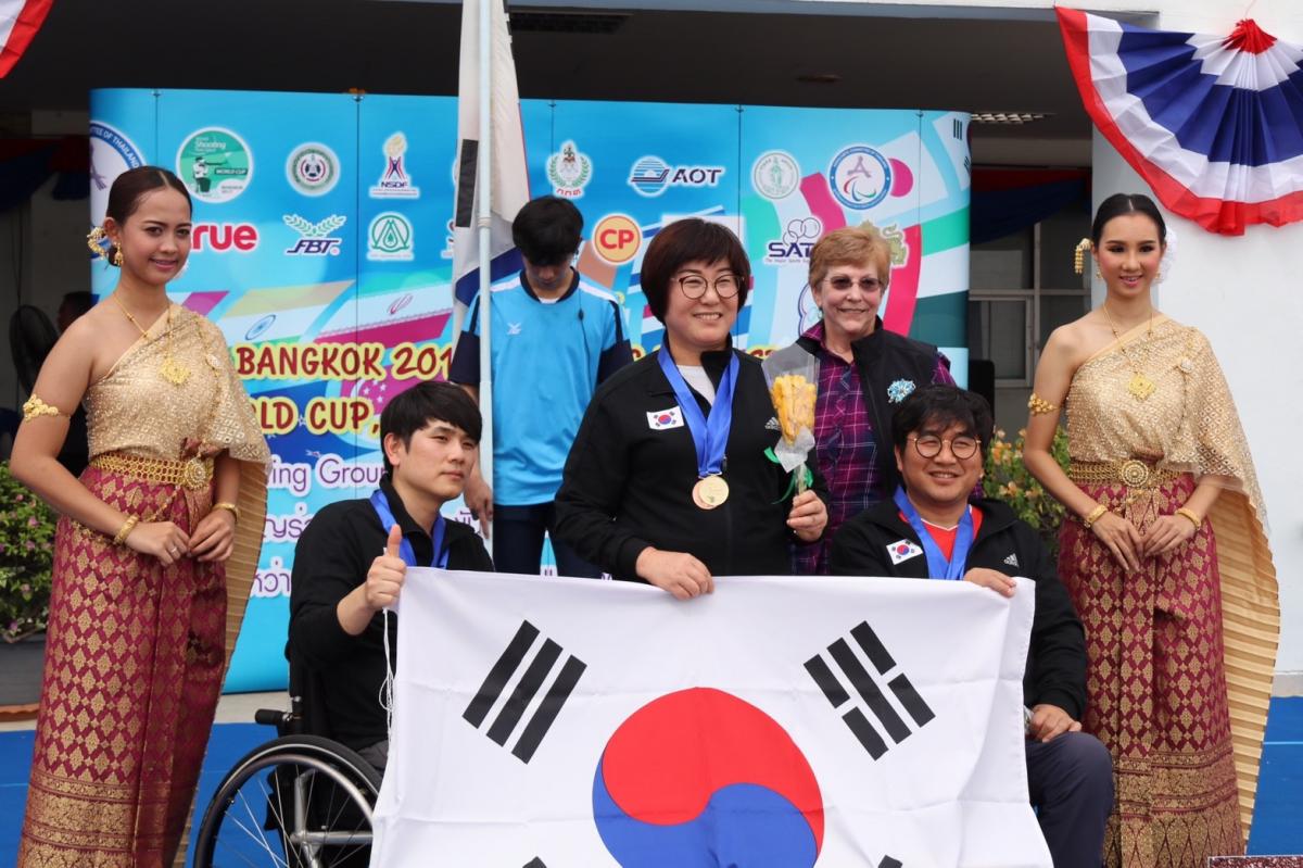 three South Korean shooters with their medals and their flag