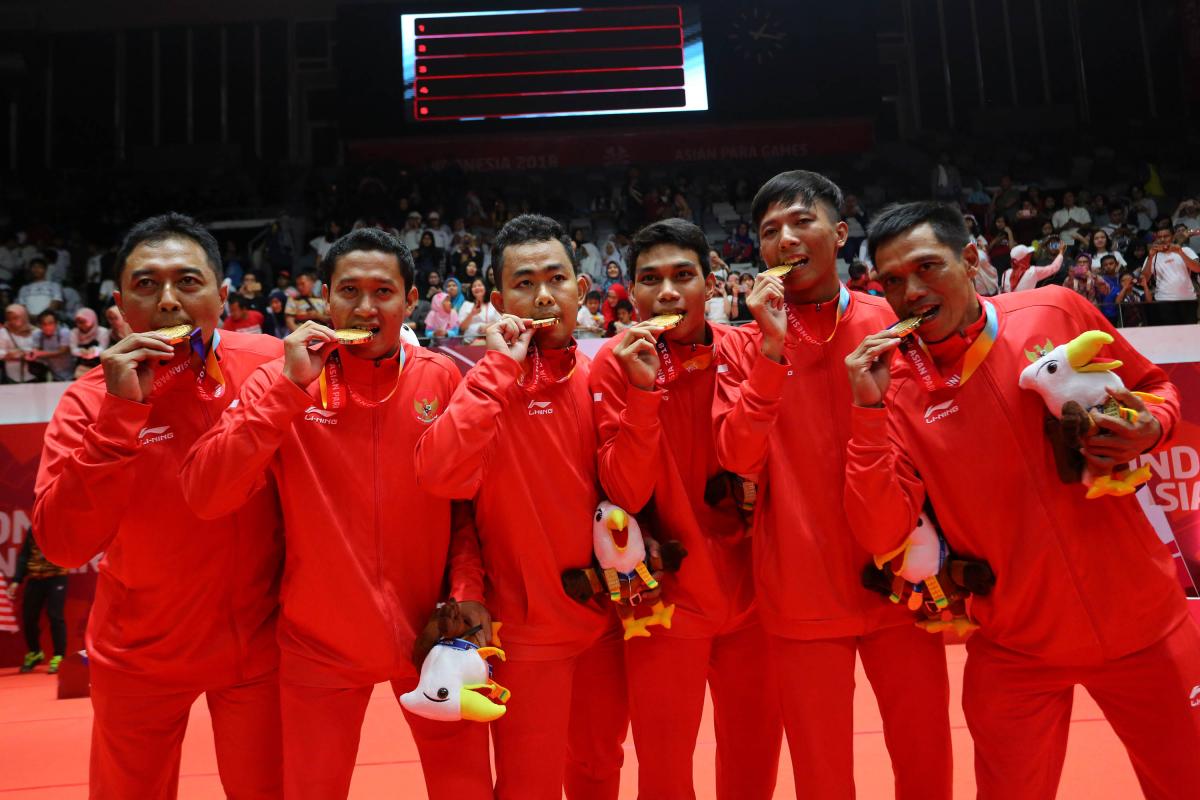 a group of Indonesian male Para badminton players biting their gold medals