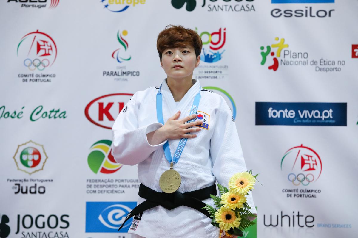 female judoka Soohee Choi holds her hand over her heart on the podium with a gold medal round her neck