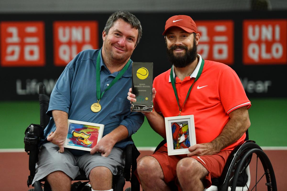 Two men in wheelchair tennis holding a trophy on a tennis court
