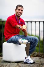 A picture of a man sit down and showing his gold medal