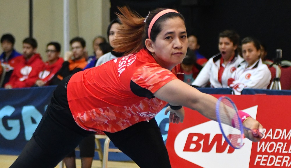 A female Para badminton player leans down to hit a forehand