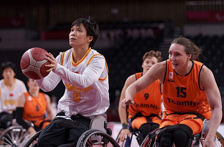 Chinese female athlete tries to shoot basketball while Dutch athlete looks on