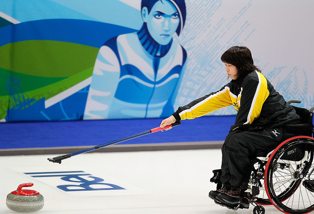 Female wheelchair curler releases stone in front of mural backdrop