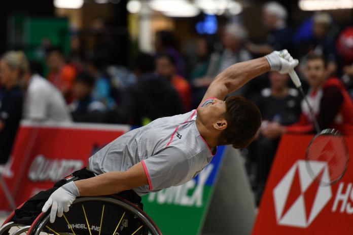 a male wheelchair badminton player leans back to hit a shot