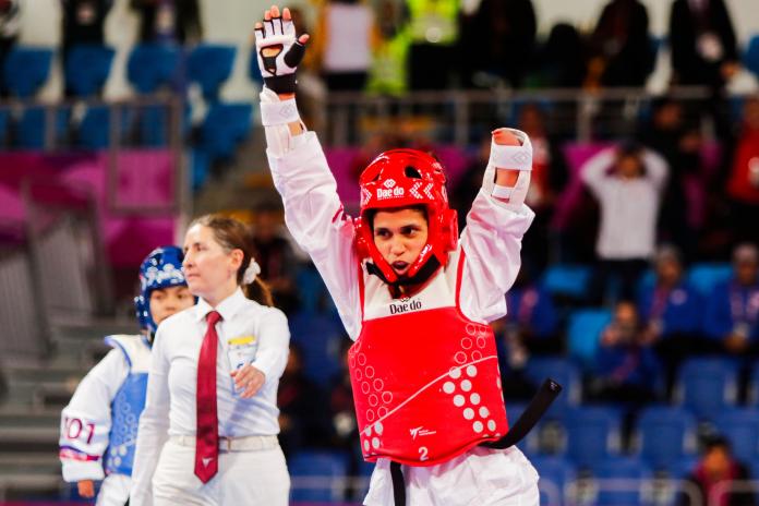 a female Para taekwondo athlete raises her arms in celebration