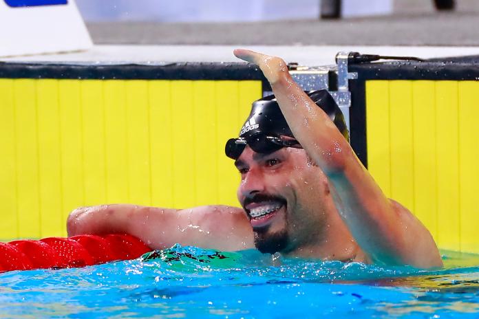 a male Para swimmer raises his arm in celebration in the pool