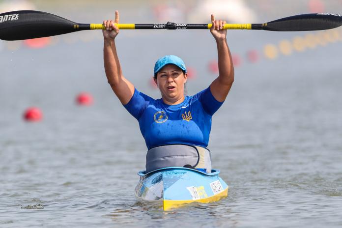 Woman in kayak raises paddle over her head