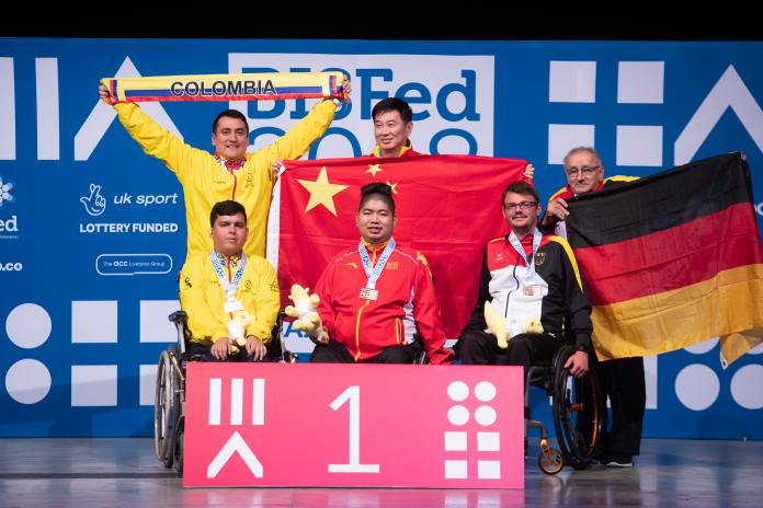 Three boccia athletes and their assistants pose on podium 