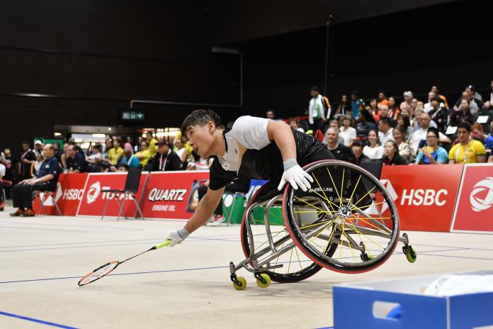 South Korean man in wheelchair leans over to hit the badminton birdie