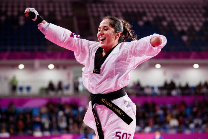 a female Para taekwondo athlete raises her arms in celebration