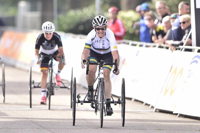 Australian woman in tricycle sprints toward finish line with opponent behind her