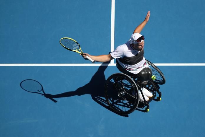 Dylan Alcott on the court extending his arms in celebration while holding the racket