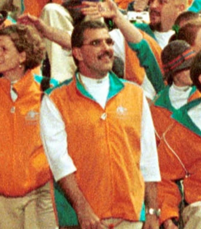 A man in orange uniform smiles in a crowd during the Opening Ceremony of the Sydney 2000 Paralympic Games.