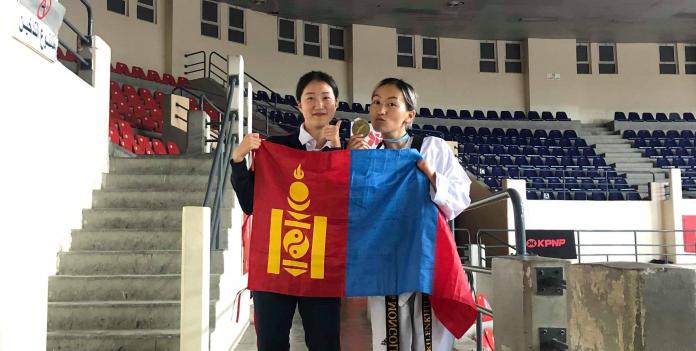 Female taekwondo athlete hold Mongolian flag with friend and her medal