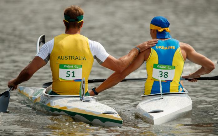 Two men after a canoe race supporting each other's boats