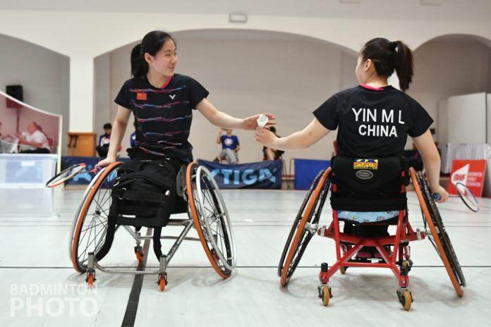 One Chinese female wheelchair badminton player hands her teammate the shuttle