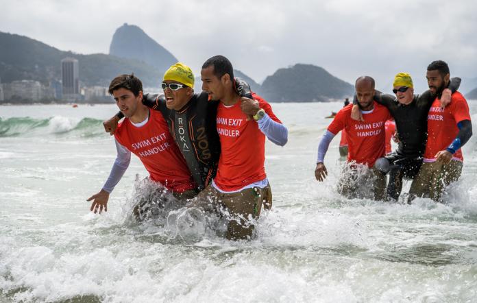 Two male handlers help a male triathlon transition from the water phase