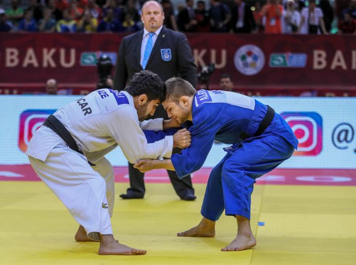 Two judoka put their heads together and hold each other, trying to pull one down