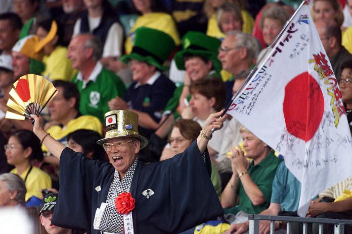 Japanese fan dressed in traditional clothing and holding Japan flag as he cheers on a judo competition