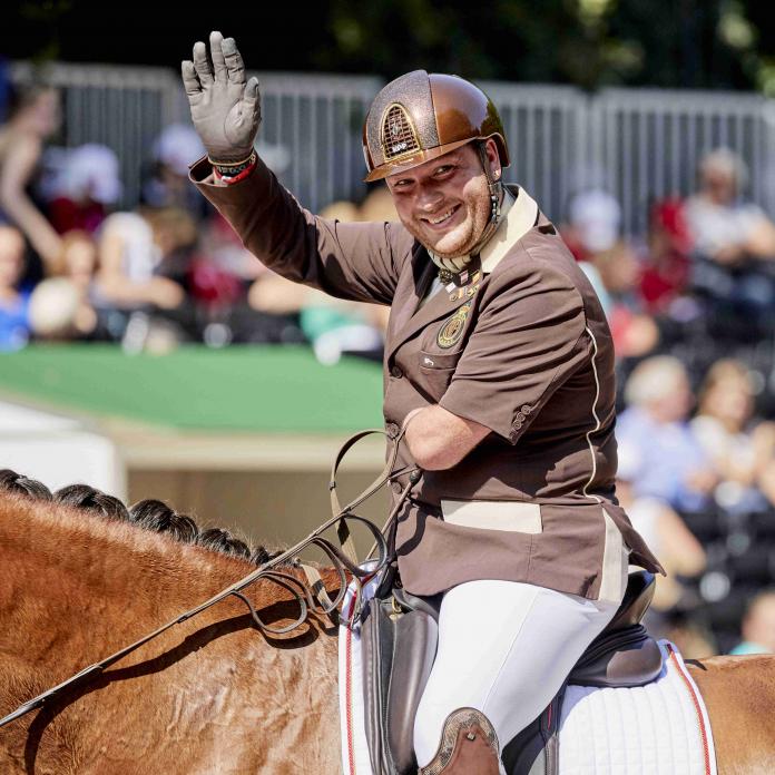 Man on horse with left arm amputation waves at crowd