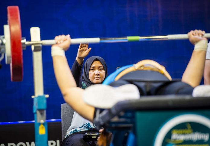 Woman referee behind a powerlifter signals a good lift