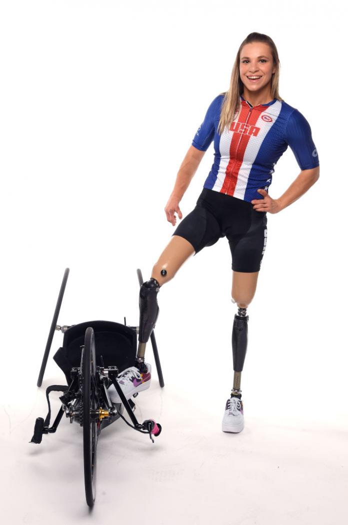 A woman with two legs amputated poses next to a hand bike