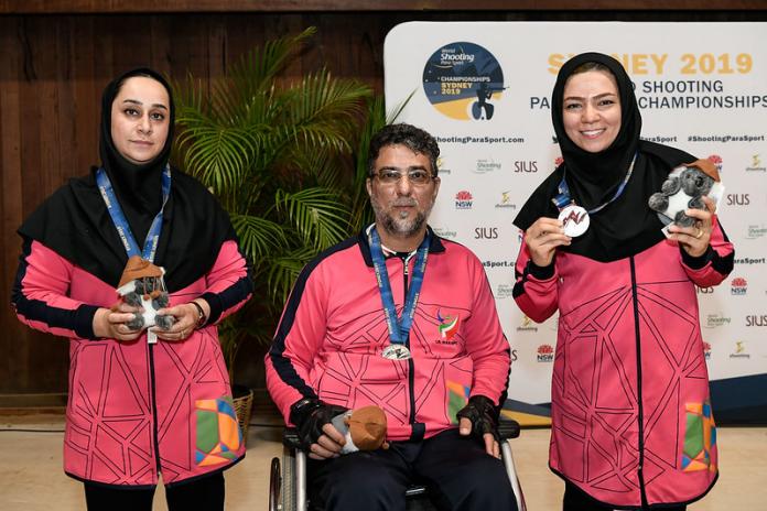 Three athletes on the Iranian shooting Para sport team smile for a photo on the podium