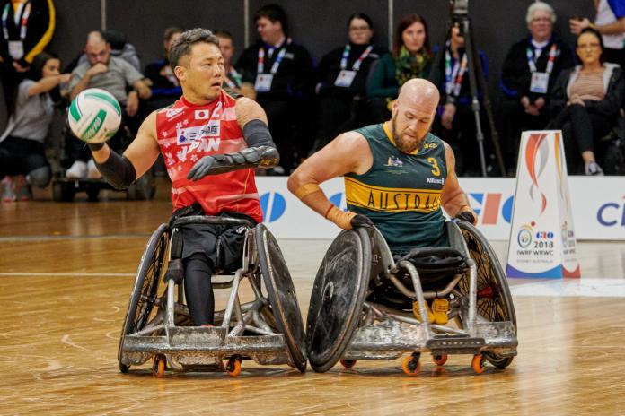 Japanese wheelchair rugby player ​​​​​​​Yukinobu Ike holds the ball while Australian player Ryley Batt tries to stop him