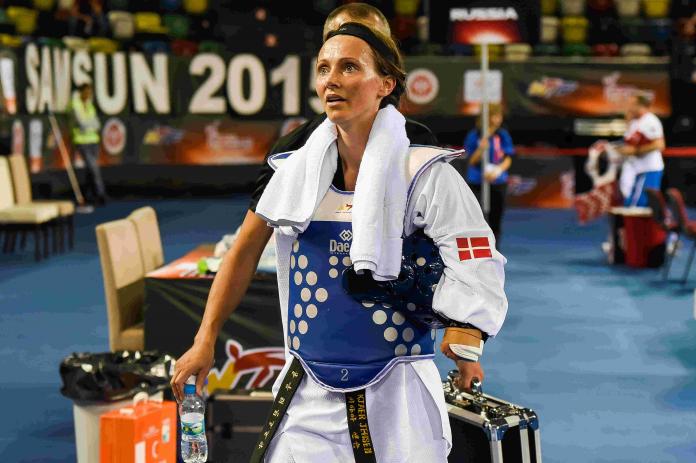 Female taekwondo athlete with right arm impairment walks off away from matt