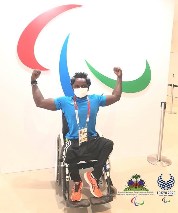 Ywenson Registre Haiti in his wheelchair, flexing his arm muscles, in front of the Agitos