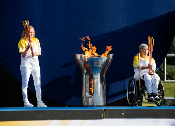 Two people holding torches with the Paralympic cauldron and flame in between