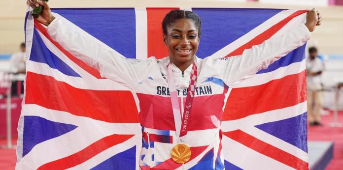 Kadeena Cox smiles with the gold medal hanging around her neck while holding the British flag