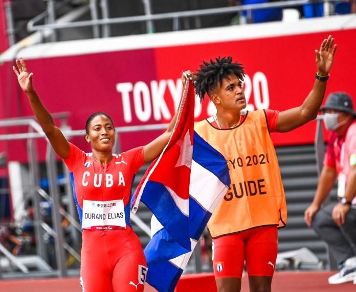 Omara Durand lifts her arms to celebrate next to her guide after winning her sixth Paralympic gold