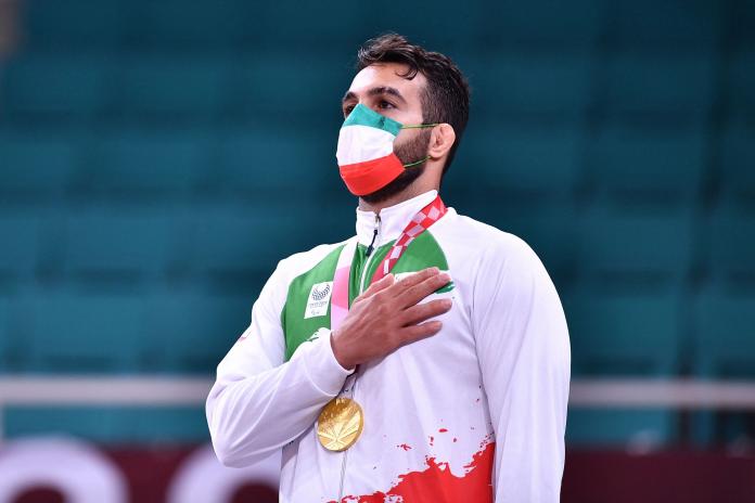 Iranian judoka Vahid Nouri with his gold medal hanging around his neck and his hand on his chest while listening to the Iranian national anthem