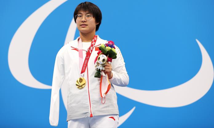 A woman poses with a gold medal, holding the mascot in her left hand