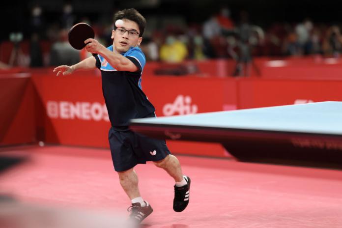 Male table tennis player reaches to return a shot